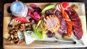 A fall harvest inspired charcuterie board shot from above. The board contains different cheese, cured meats, season fruits and veggies, and candied walnuts.