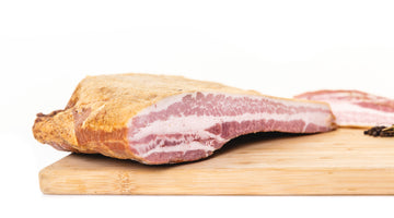 The cross section of a bacon slab on a cutting board to show the fat to meat ratio.