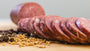 A closeup of il porcellino salumi Summer Sausage slices, herbs and spices, and a whole summer sausage chub in the background.