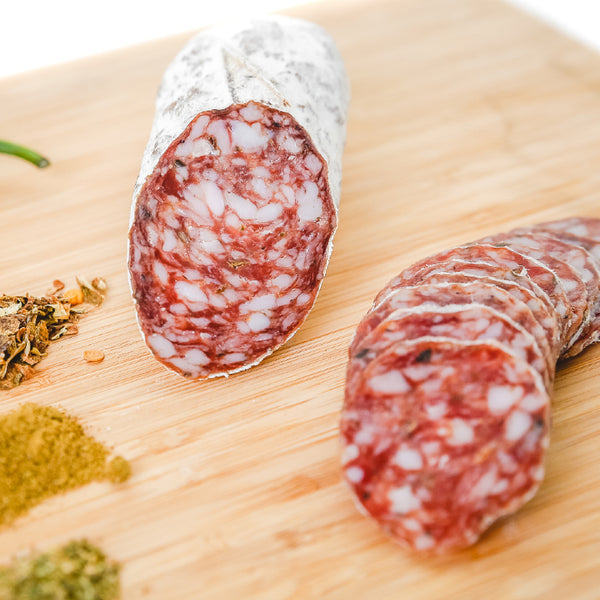 A close up picture of a cross section of green chile tequila salami on a cutting board.