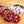 Load image into Gallery viewer, A close up of salami slices displaying the fat marbling, herbs and spices. The salami slices are on a wood cutting board with herbs and spices blurred in the background.
